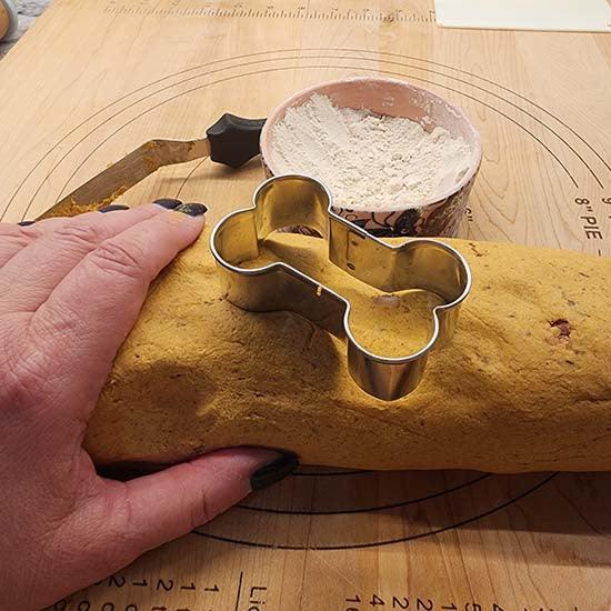 Hand cutting dog treat dough with bone-shaped cutter, gluten-free pupcake ingredients nearby
