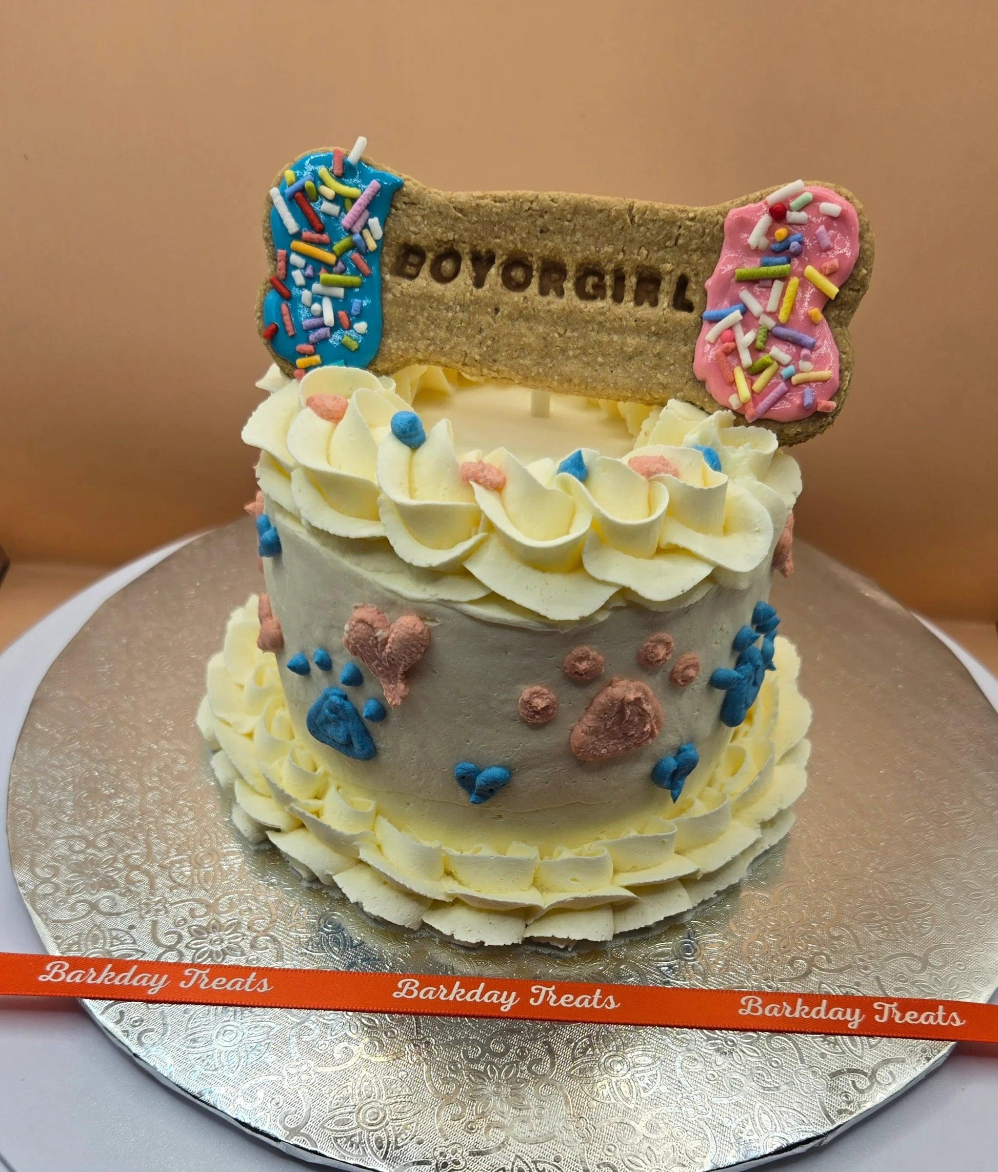 Barkday Treats dog gender reveal cake with cream cheese frosting, pink and blue paw print decorations, and a Boy or Girl bone cookie topper with sprinkles