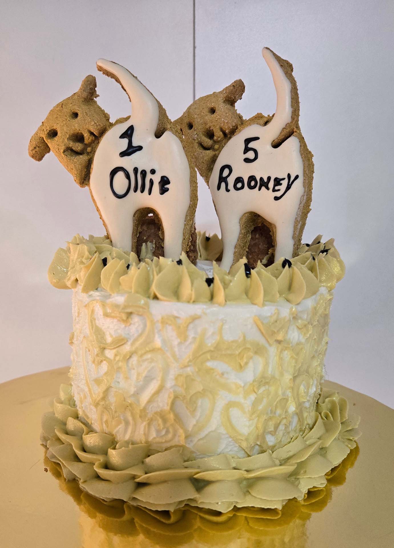 Decorative cake with dog-shaped candles and '1 Ollie' and '5 Rooney' text on dog shaped cookies